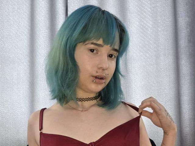 TeraHammar with teal-blue hair, nose ring, lip piercings, choker, red bra, holding strap, tattoo on right hand, pale skin, looking at camera.