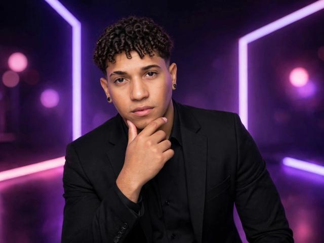 Yoximanuelprime with short, curly black hair, brown eyes, and ear gauges, wearing a black suit, hand on chin, looking serious, neon pink and purple lights in background.