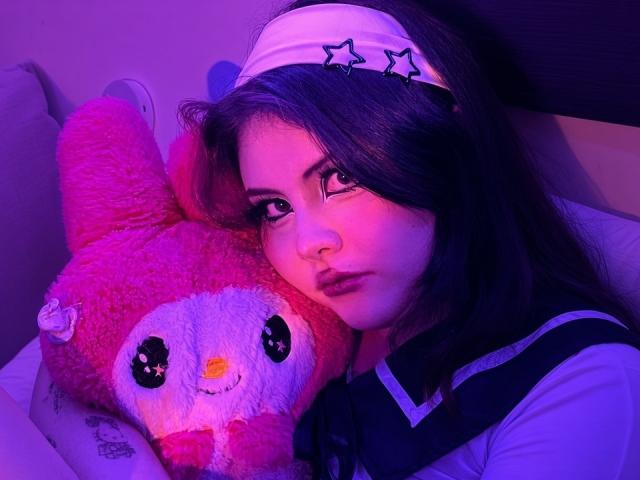 MicheMeow with purple-tinged face, holding pink fluffy bunny stuffed animal, wearing white headband with stars, and navy blue sailor-style shirt, looking serious.
