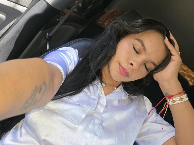 Yurimy with closed eyes, black hair, white shirt, small tits, tattoo on arm, red bracelet, hand in hair, smiling, car interior, soft light.