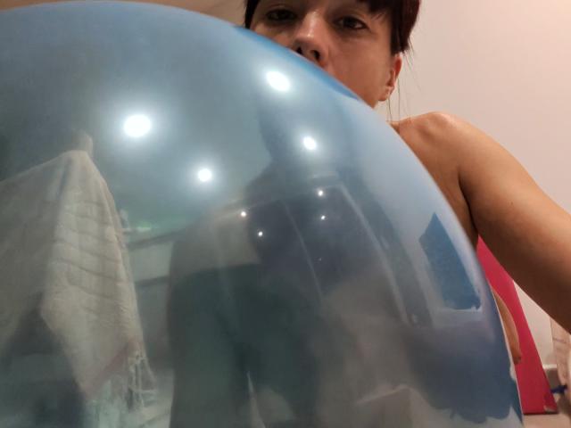 OrianaLaFrancaise tiene davanti a sé una palla gonfiabile blu, con i suoi seni scoperti parzialmente visibili e il viso che spunta dalla parte superiore. Ha i capelli rossi..