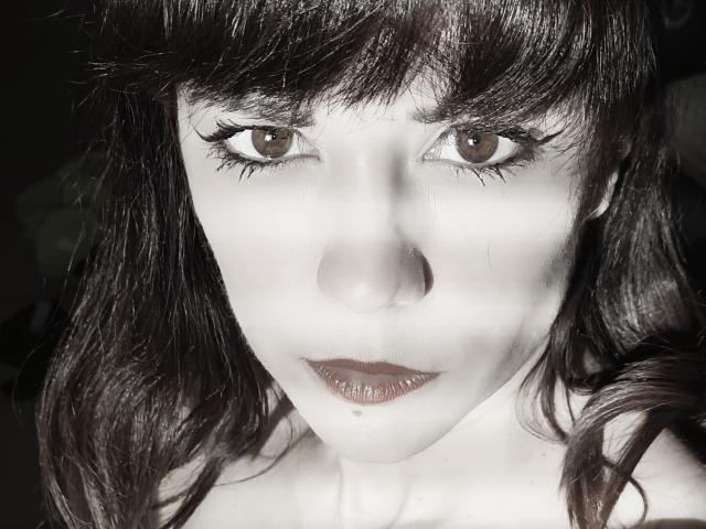 OrianaLaFrancaise has dark brown eyes, thick black eyelashes, and wavy brown hair with bangs. She's wearing dark lipstick, and her white skin contrasts with her dark hair.