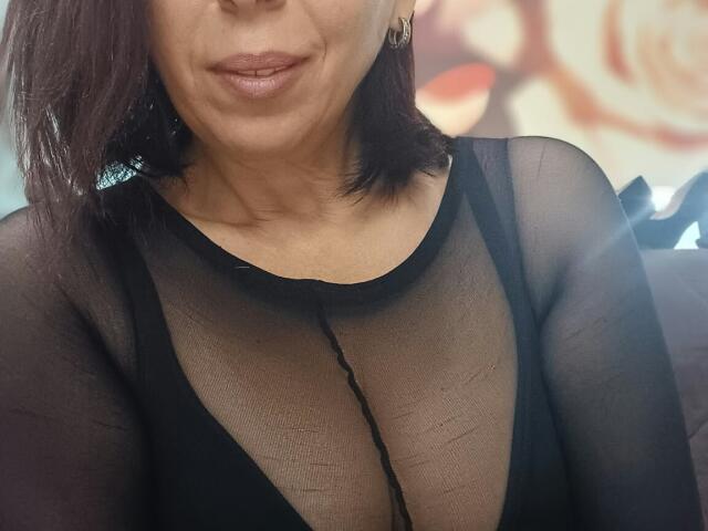 LauraSin with medium brown skin, short brown hair, and pink lipstick, wearing a sheer black top, showing her tits through the fabric, slightly smiling.