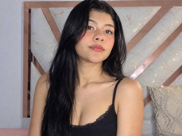 SweetAmanhda with long black hair, wearing a black lace-trimmed tank top, showing her tits and a cute face with pink lips, looking slightly to the right.