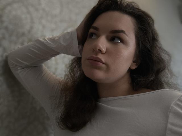 Dreia a les cheveux bruns ondulés, porte une chemise blanche à manches longues et a une expression sérieuse, avec sa main dans ses cheveux, et regarde sur le côté. Ses seins sont légèrement visibles..