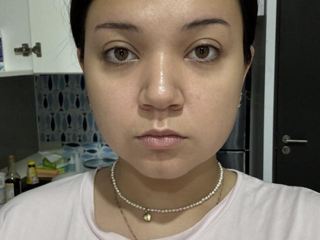O rosto de KaylaFerard está brilhante, com olhos castanhos e um leve semblante de beicinho, usando um colar de pérolas e uma camisa rosa. Suas nádegas não estão visíveis, apenas seu rosto e parte superior do peito..