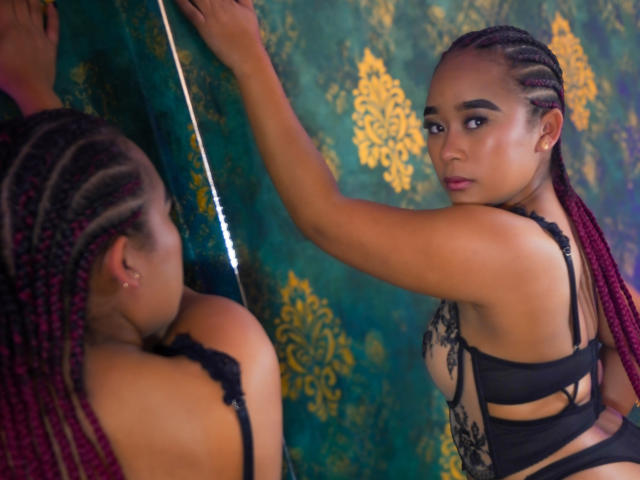 KailaniMoani with red braided hair, black lace lingerie, looking at herself in a mirror, showing her ass and tits, in a sensual, reflective pose.