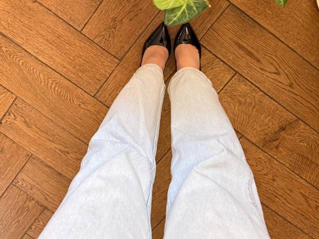 Teffi's legs in light blue jeans and black pointed shoes standing on wooden floor, with a green leaf at the top of the frame.