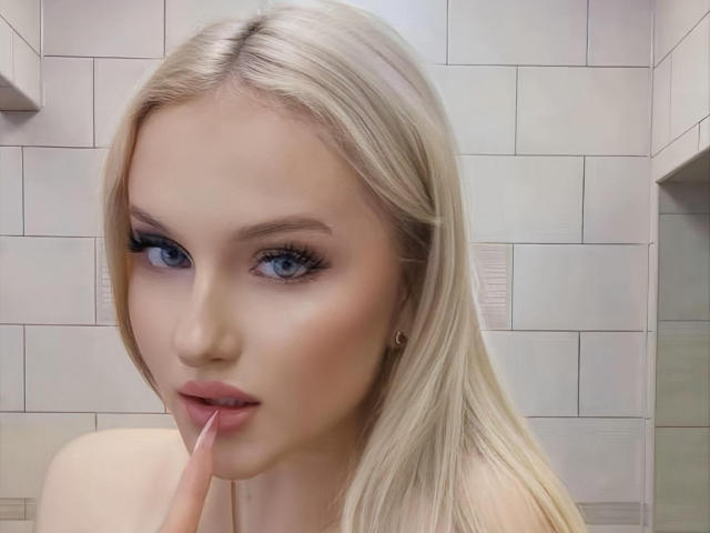 SimonaKorzep has blonde hair, blue eyes, and is sucking on her finger with her pink lipstick slightly parted. She's wearing a small hoop earring on her left side.