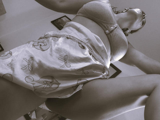 AmberDemons with big tits in a bra and white shorts with butterfly patterns, viewed from below, showing her ass and legs, in a sepia-toned image.