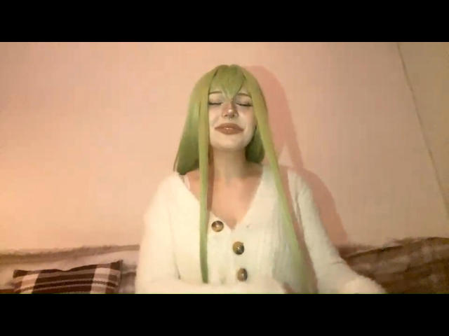 KinEvi with green hair, eyes closed, wearing a white cardigan with buttons, has a relaxed, content expression, sitting on a brown and white striped couch.