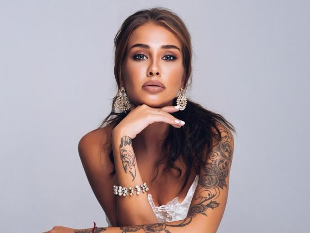 Kissamya a la peau mate, les yeux marron et de longs cheveux bruns attachés en queue de cheval. Elle porte de la dentelle blanche, de grandes boucles d'oreilles et un bracelet de perles. Son bras tatoué repose sur son menton..