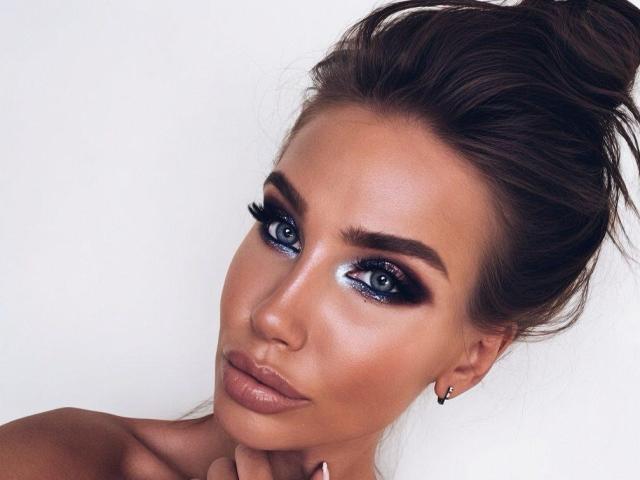 Kissamya a les yeux bleus, des sourcils foncés, un trait d'eye-liner noir intense et de longs cils. Ses cheveux bruns sont attachés en un chignon désordonné, et elle porte un rouge à lèvres nude avec un léger éclat..
