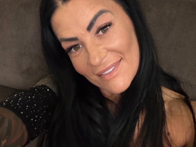 AndraD, avec ses cheveux noirs, ses sourcils épais, ses yeux marrons et un sourire dévoilant ses dents, porte une manche noire brillante, une partie supérieure du corps noire et un tatouage sur son bras..