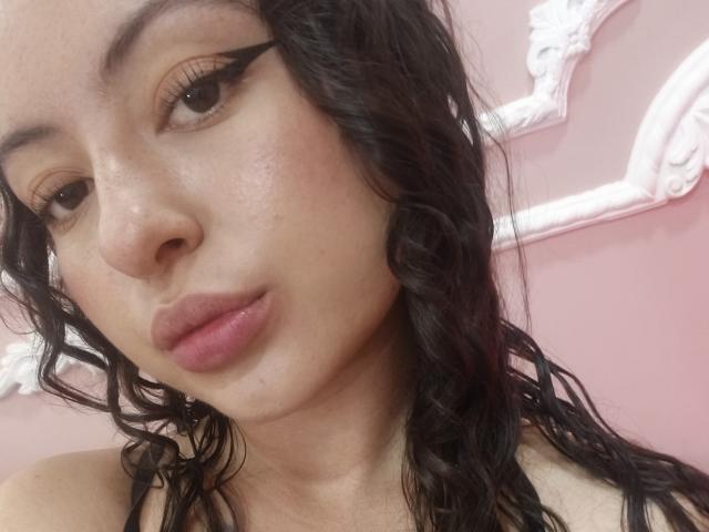 MiiaBennet has wavy black hair, thick black eyeliner, and glossy pink lips. Her light brown skin is slightly shiny, showing a natural, relaxed look. Her boobs are not visible.