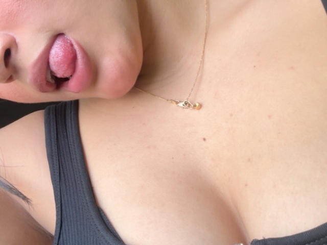 MiiaPalmer's tongue is out, showing pink, slightly glistening lips. She's wearing a black tank top, a gold necklace, and her tits are visible with a few small freckles.
