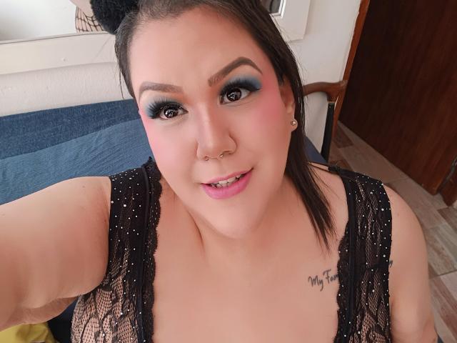 GiiannaMorrys with pink cheeks, blue eye makeup, black lace top, nose ring, and "My fit" tattoo, smiling at the camera, showing her tits. Brown hair, cute cat ears.