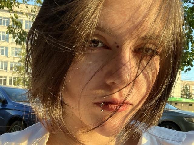 HanhFontillas has brown, messy hair with sunlit strands, a pierced lower lip, and a small mole on her right cheek. She's wearing a white shirt, outdoors.