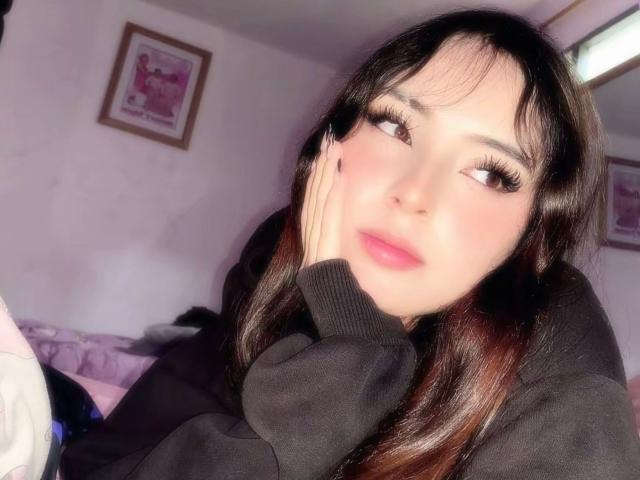 GigiOchoa, con cabello negro largo, labios rosados y pestañas gruesas, vestida con una sudadera negra, con el mentón apoyado en la mano, mirando hacia un lado, en una habitación luminosa..