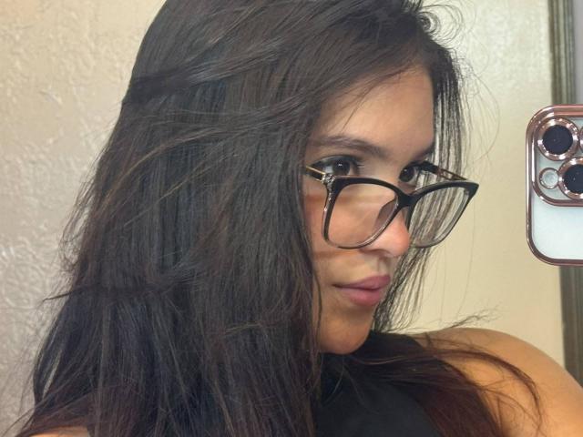 KatarinaNovak with long, dark brown hair, wearing black glasses, taking a mirror selfie with a phone in her right hand, showing her pouty lips.