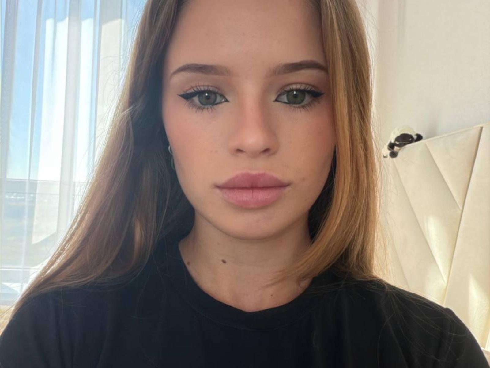 RafelaHosack a les yeux vert clair, des lèvres roses et pleines, et de longs cheveux bruns. Elle porte du maquillage noir avec un trait d'eye-liner ailé, une chemise noire, et a une petite tache de naissance sur le cou..
