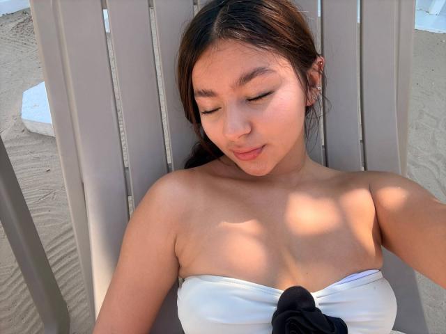 AlessiaFerry with closed eyes, lying on a beach chair, wearing a white strapless top, showing her bare shoulders and small black bow in the center.