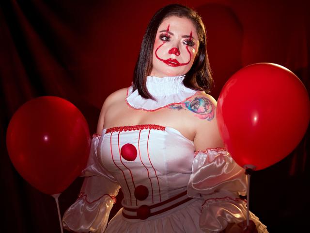 SamanthaVenus with red clown makeup, white off-shoulder dress, holding red balloons, medium tits, black bob haircut, tattoo on right shoulder, red lipstick, dark red background.
