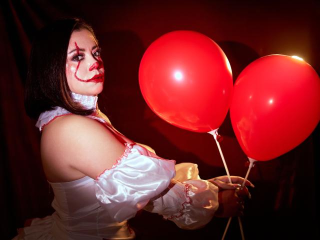 SamanthaVenus with white off-shoulder dress, red makeup, holding two red balloons, dark hair, looking back, lit from side, white neck scarf, glossy skin, dark background.