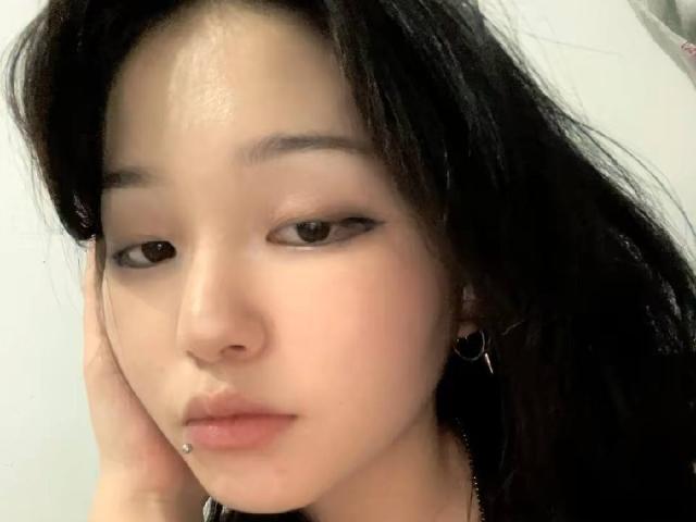 PeiBlank tiene la piel clara, cabello negro y un piercing en el labio inferior. Está mirando hacia abajo con una mano en la mejilla, y lleva delineador de ojos..