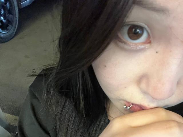 PeiBlank's face with brown eyes, black hair, and a lower lip piercing, holding her chin. Her nose is slightly pink. Motorcycle tire in the background.