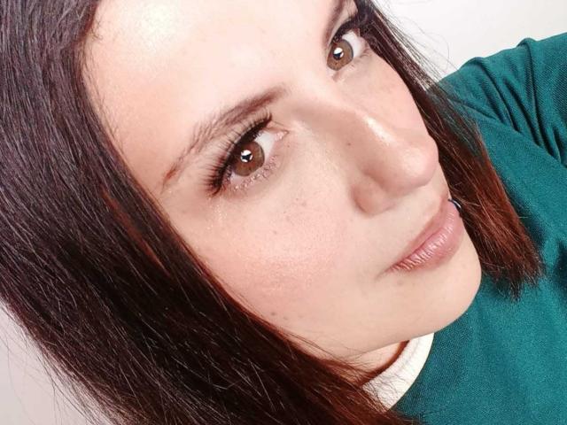 MaryCruzz's face, showing brown eyes, dark straight hair, green shirt, and slightly parted lips with a subtle pink lipstick, in a close-up selfie.