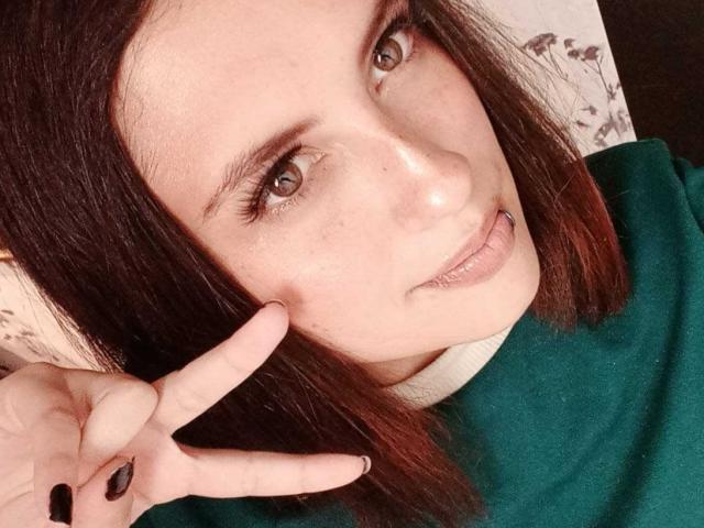 MaryCruzz heeft een bleke huid, bruine ogen en een klein piercing in haar neus. Ze maakt een vrede-teken met haar rechterhand, draagt een groene top en heeft bruin haar..
