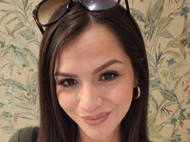 CameronViviane has brown eyes, long dark hair, and is wearing black sunglasses on her head. She's smiling with pink lips, small nose, and gold hoop earrings.