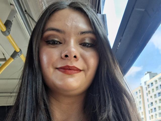 KatherinLatin ha una pelle luminosa, capelli neri e lisci, e indossa rossetto rosso con eyeliner ad ali di farfalla. Il suo naso è adorabile e sta sorridendo leggermente. La sua vulva non è visibile..