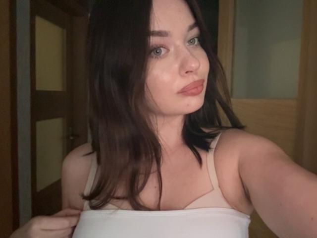 Kiara, avec sa peau claire, ses yeux verts et ses cheveux bruns foncés, porte un débardeur blanc, laissant entrevoir sa petite poitrine et un léger décolleté sur une photo d'elle-même..