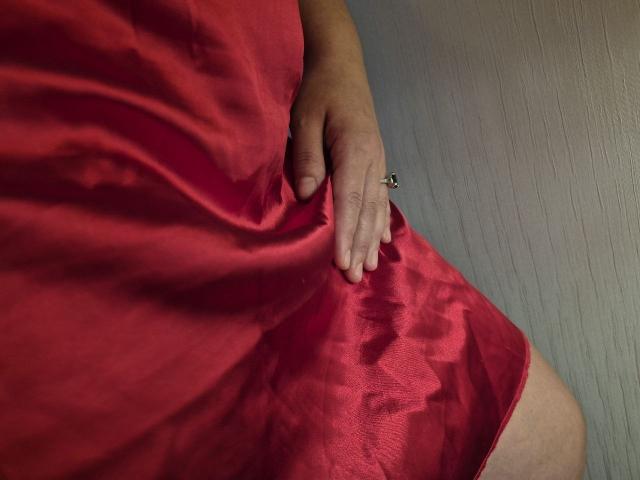 Dinastiia's hand resting on her red, silky, wavy-dress-covered ass. She wears a silver ring on her finger. Her thigh is visible. Image shows her lower torso.