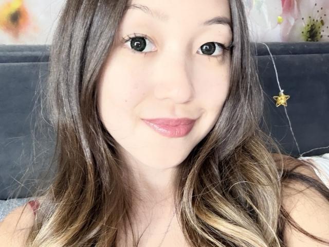RenyLime has light skin, green eyes, and long brown hair with blonde highlights. She's smiling with pink lipstick and a slight blush, wearing a sleeveless top.