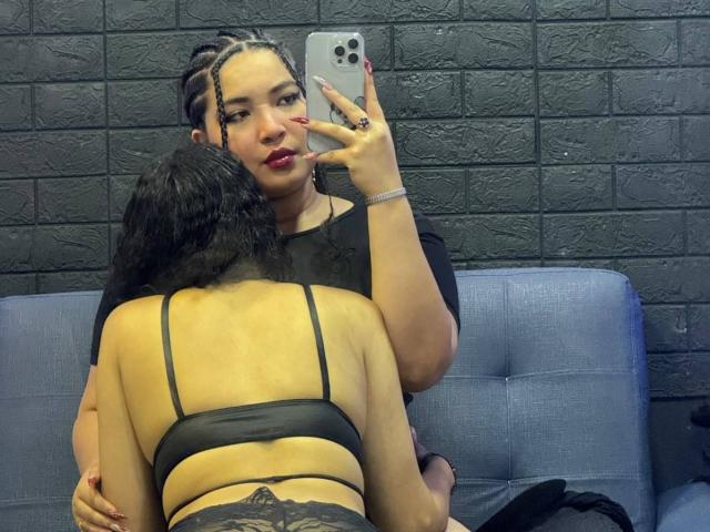 CharlotteTiffany with braided hair, red lipstick, black top, taking selfie, holding phone, sitting on blue couch, with her back to camera, wearing black lace bra, holding her ass.