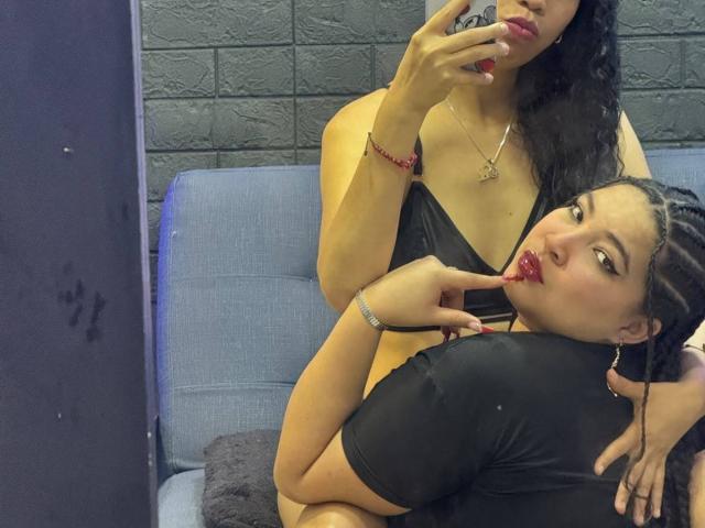 CharlotteTiffany with curly black hair, black bikini top, and red lipstick, sucking her finger, while another CharlotteTiffany with braids, black shirt, and red lipstick, kisses her finger.