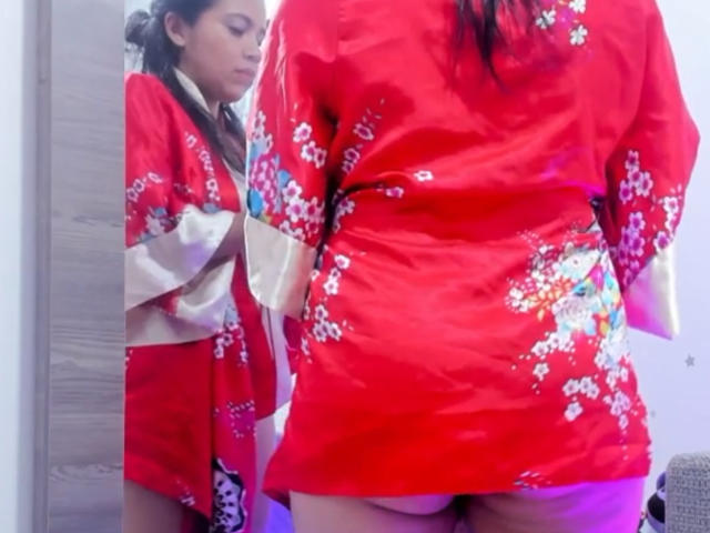 VickyRousse wearing a red floral kimono, reflection in mirror, her butt and pussy slightly exposed, red kimono with white and beige accents, dark hair, bedroom setting.