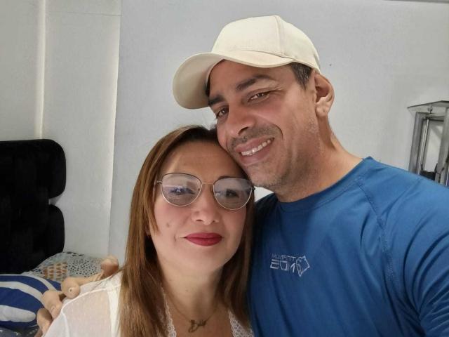 VictoriaSexOne with glasses and red lipstick, and a guy in a white cap and blue shirt, smiling at the camera. He's got a cute ass and she's got nice tits.