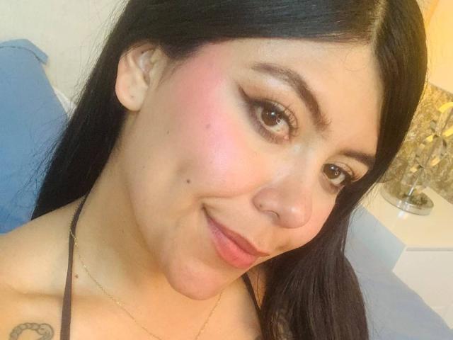 CatalinaReiyna has pink cheekbones, long black hair, brown eyes, and a subtle smile. She's wearing a black halter top with a small tattoo on her right shoulder.