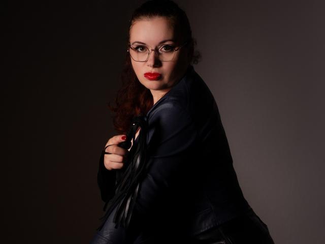 ElisabethLovee, com cabelo castanho encaracolado, batom vermelho, óculos, jaqueta de couro preta, segurando um chicote de couro preto, olhando para a câmera, fundo escuro, sexy, confiante..