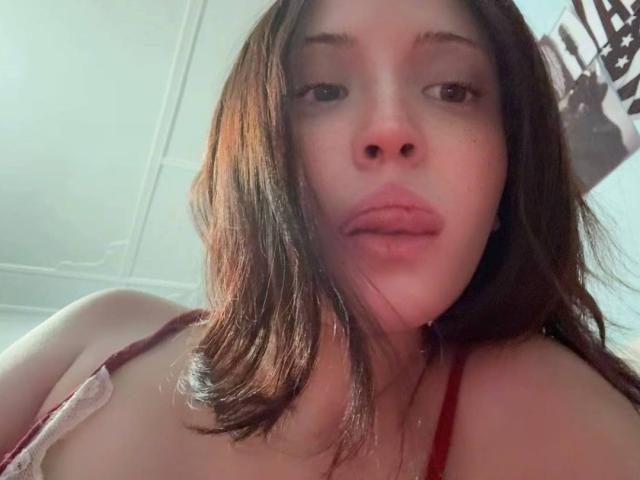 ElaneBoth has medium-length brown hair, light skin, and is wearing a red strap, showing her bare shoulders and slightly open mouth in a low-angle selfie.