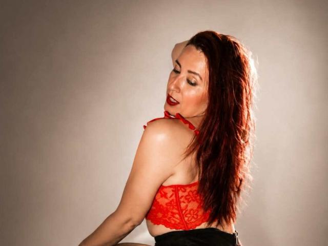 SweettEve with red lace bra, showing her tits, back to camera, red hair, closed eyes, red lipstick, black skirt, soft lighting, slight smile, sexy pose.