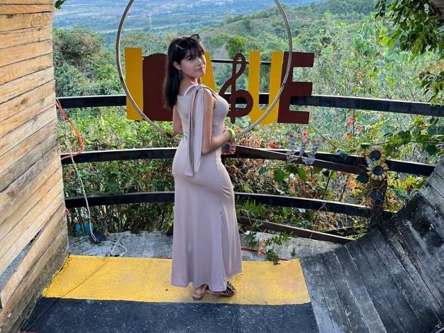 AshlyLee in a pink, form-fitting dress with a side slit, showing her ass and standing on a yellow and black platform, looking over her shoulder.