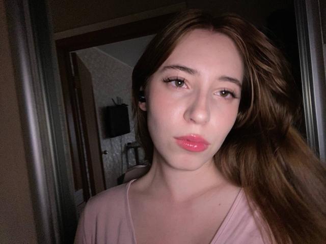 AleneFalcioni has puffy pink lips, light skin, and long brown hair. She's wearing a pink top, looking directly at the camera with a slightly pouty expression.