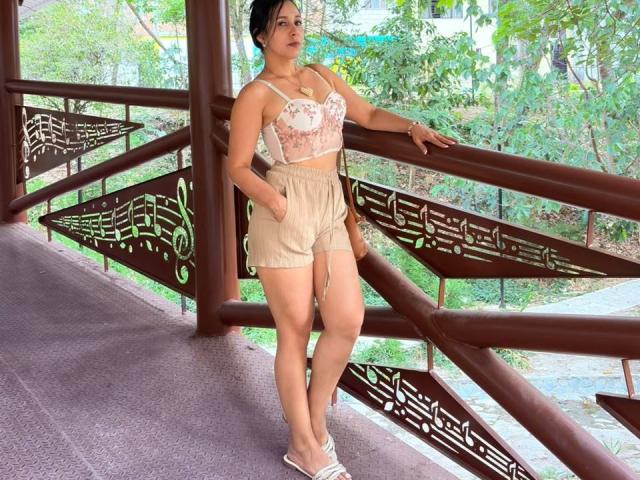 KattyRivera stands in a brown metal bridge, wearing a floral bralette, beige high-waisted shorts, and white flip-flops, with her hands in pockets, showing her ass and tits.