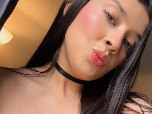 EmmaLombardi has puffy pink lips, a black choker, and wet skin. Her dark hair is straight, and her cheeks are flushed. Her eyes are half-closed.