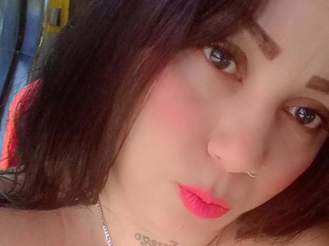 VictoriaLands has pink lipstick, a nose ring, and a tattoo below her neck. Her black hair and blue eyes are prominent. Her face is slightly flushed.
